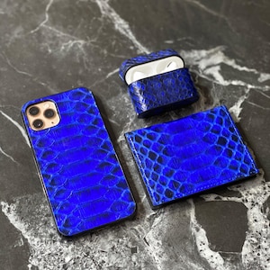 May include: A collection of blue leather accessories featuring a snake-like pattern. The set includes a phone case, an AirPod case, and a cardholder. The phone case is designed for a smartphone with a gold camera module.