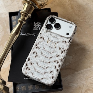 May include: White and brown snakeskin-textured phone case with the initials "WAL" embossed on the back. The case is displayed in a black box with a gold-colored decorative object in the background. The case has a camera cutout.