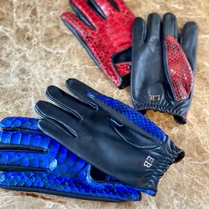 May include: Two pairs of leather gloves with a snakeskin pattern. One pair is black with blue snakeskin and the other is black with red snakeskin. The gloves have the initials "BB" and "LR" embroidered on them.