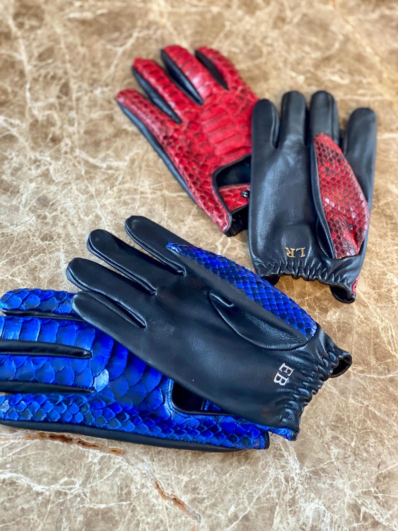 May include: Two pairs of leather gloves with a snakeskin pattern. One pair is black with blue snakeskin and the other is black with red snakeskin. The gloves have the initials "BB" and "LR" embroidered on them.