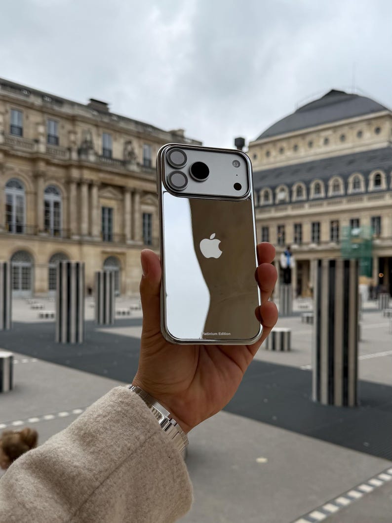 Puede incluir: Una funda plateada para iPhone con parte trasera reflectante, con el logotipo de Apple. La funda tiene un marco met&aacute;lico y un recorte para la c&aacute;mara. Las palabras "Platinum Edition" est&aacute;n impresas en la parte inferior.