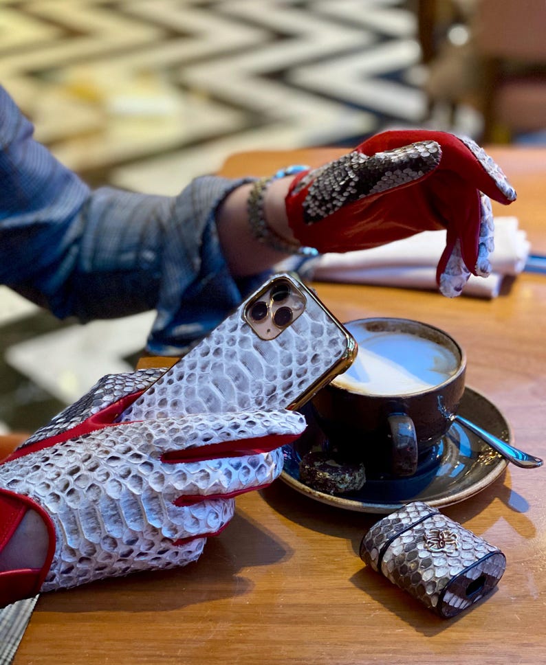 May include: A pair of red and white snakeskin gloves with a white snakeskin phone case and a matching snakeskin case for wireless earbuds.