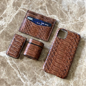May include: A set of brown leather accessories, including a cardholder with a Visa card, a phone case, a lighter case, and a small case. The items have a textured, reptile-like pattern.