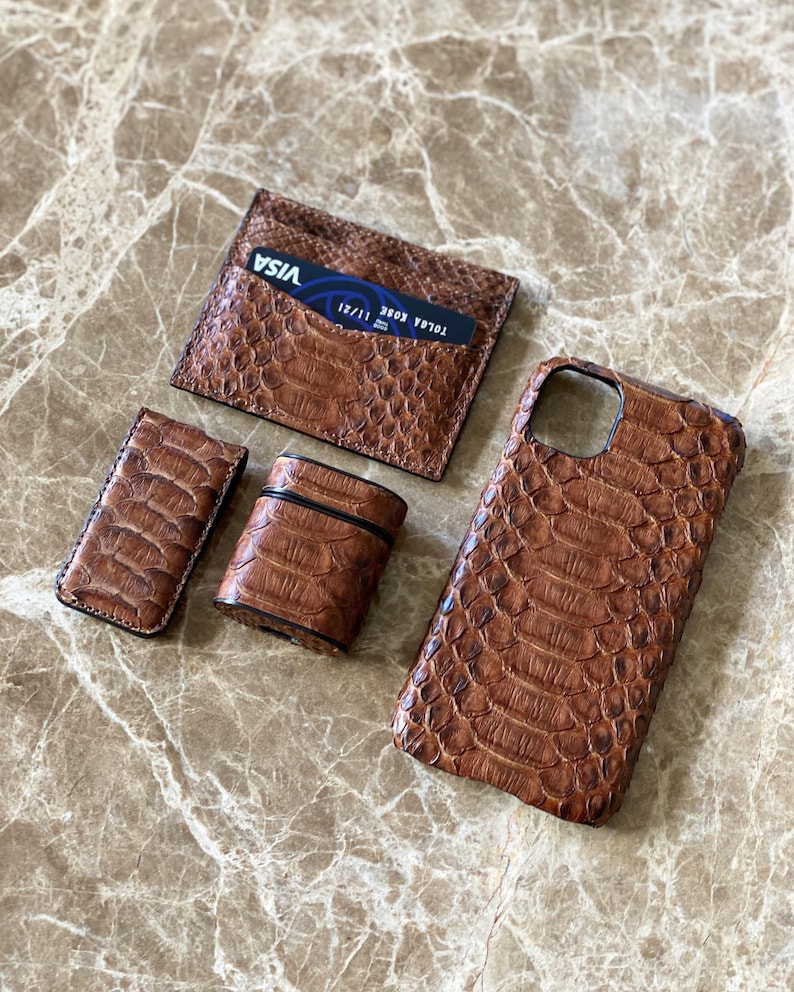 May include: A set of brown leather accessories, including a cardholder with a Visa card, a phone case, a lighter case, and a small case. The items have a textured, reptile-like pattern.