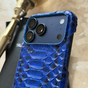 May include: A blue snakeskin-textured phone case with a black camera module. The case has a textured, scaly pattern in shades of blue and black. The phone case is designed to fit a smartphone.