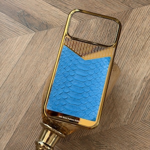 Peut inclure: Une coque de téléphone rectangulaire avec un cadre en or poli et une incrustation en peau de python texturée bleu vif. La partie supérieure présente un motif chevron doré, tandis que le bas porte l'inscription 24k Gold Python Edition.