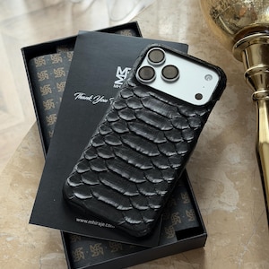 May include: Black textured phone case with a scale-like pattern, resting on a black box. The case has a camera cutout and is next to a box with the text "Thank You". The box has a repeating pattern and the website address www.mhiraje.com.