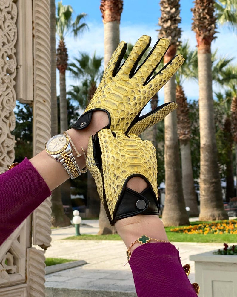 May include: A pair of yellow leather driving gloves with black accents and a snakeskin pattern.