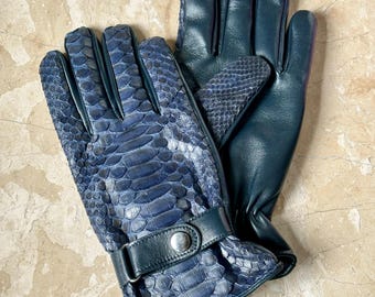 Pode incluir: Um par de luvas de couro azul escuro. As luvas apresentam um padrão de pele de cobra na parte superior e couro liso na palma. Uma tira azul escura com um botão prateado prende o pulso.