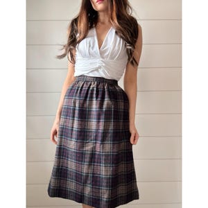 May include: A white wrap top and a knee-length plaid skirt. The skirt has a tartan pattern in brown, navy, and burgundy. The outfit is a vintage style, suitable for a casual or semi-formal occasion. The skirt length is approximately 76 cm.