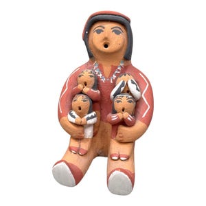 Puede incluir: Figura de cerámica de color terracota que representa una figura que sostiene tres figuras más pequeñas. La figura principal lleva una camisa roja con detalles blancos y una gorra negra. Las figuras más pequeñas tienen las manos cerca de la boca. Tema nativo americano.