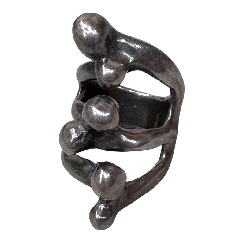 Puede incluir: Un anillo plateado con un dise&ntilde;o abstracto. El anillo presenta una serie de formas redondeadas interconectadas, creando una apariencia &uacute;nica y escultural. El metal tiene una superficie ligeramente texturizada, agregando profundidad al dise&ntilde;o.