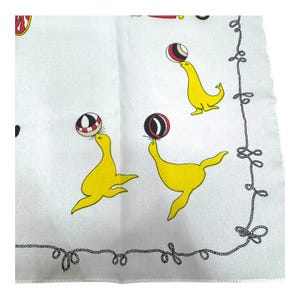 May include: White fabric with a repeating pattern of yellow seals balancing red, black, and white balls. A black rope-like border frames the design. The seals are in various poses, creating a playful and whimsical aesthetic.