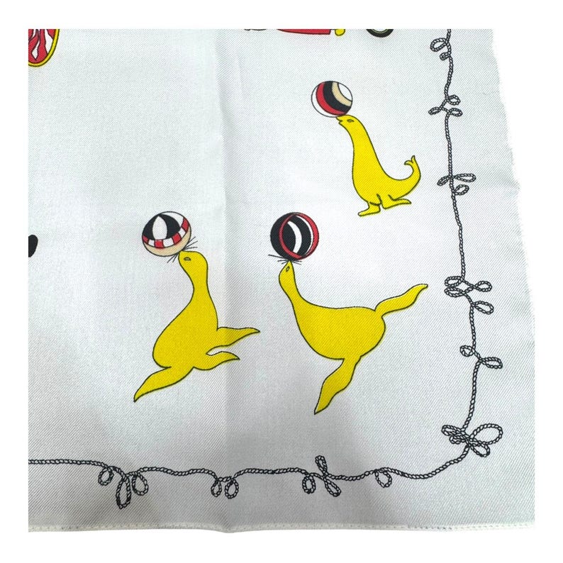 May include: White fabric with a repeating pattern of yellow seals balancing red, black, and white balls. A black rope-like border frames the design. The seals are in various poses, creating a playful and whimsical aesthetic.