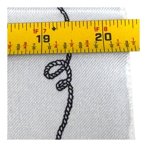May include: Close-up of a white fabric with a black rope design. A yellow tape measure shows a measurement of 19 to 20 inches. The fabric has a textured appearance.