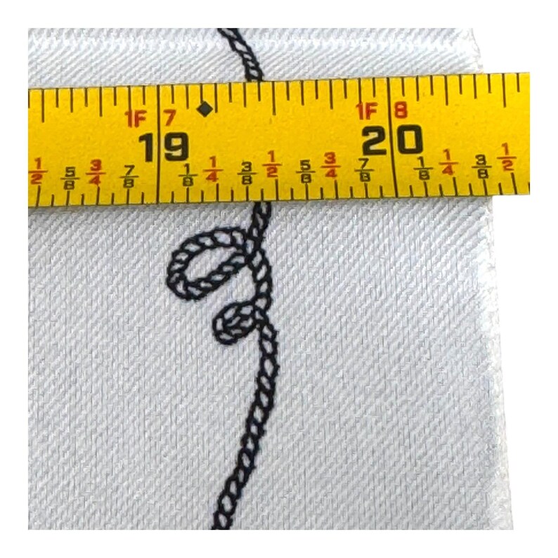 May include: Close-up of a white fabric with a black rope design. A yellow tape measure shows a measurement of 19 to 20 inches. The fabric has a textured appearance.