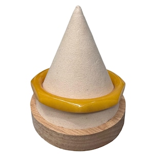 May include: A bright yellow, faceted bangle bracelet displayed on a cream-colored cone-shaped stand. The bracelet has a geometric design and is made of a glossy material. The stand is set on a round, wooden base.