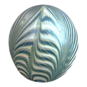 Può includere: Una sfera decorativa in vetro con un motivo a spirale di blu, bianco e argento. Il design ricorda una piuma o un'onda stilizzata, creando un effetto strutturato e iridescente. L'oggetto è un elemento decorativo.