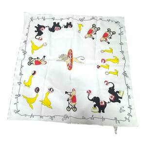 May include: White handkerchief with a circus theme. Features illustrations of performing seals, elephants, lions, and clowns on bicycles. The border has a gray, swirly design.