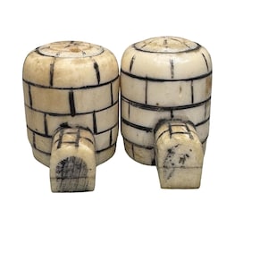 Op de afbeelding: Twee crèmekleurige, iglo-vormige decoratieve objecten met zwarte lijnen die het baksteenpatroon omlijnen. Elke iglo heeft een kleine, rechthoekige ingang. Dit zijn waarschijnlijk decoratieve items of beeldjes.