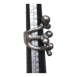 Puede incluir: Un anillo plateado con un dise&ntilde;o abstracto con formas redondeadas y l&iacute;neas fluidas. El anillo se muestra en un medidor de anillos negro, destacando su forma escultural &uacute;nica. El dise&ntilde;o del anillo recuerda formas org&aacute;nicas.