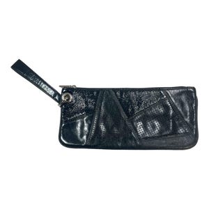Puede incluir: Clutch de cuero negro con correa de muñeca. La bolsa rectangular presenta un diseño de patchwork con secciones de cuero perforado y charol. Una cremallera y un anillo plateados detallan la parte superior.