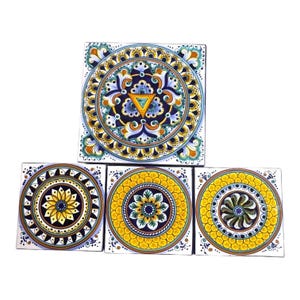May include: Set of four ceramic tiles with intricate floral designs. The tiles feature a variety of colors, including blue, yellow, green, and white. The designs are symmetrical and feature a central circle with radiating patterns.