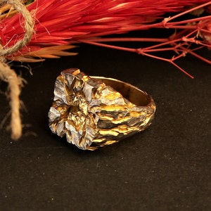 May include: A gold and silver ring with a textured, organic design. The ring is made of metal and has a rough, uneven surface.
