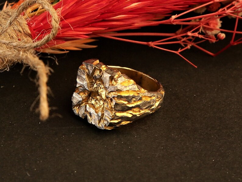 May include: A gold and silver ring with a textured, organic design. The ring is made of metal and has a rough, uneven surface.