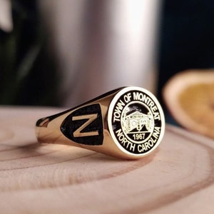 May include: Gold ring with a black enamel inlay featuring the letter "N". The ring also has a round black enamel seal with the text "Town of  Montreat North Carolina 1967".