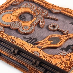 May include: A wooden box with a steampunk design featuring gears, a dragonfly, and a key. The box is closed and has a dark wood finish.