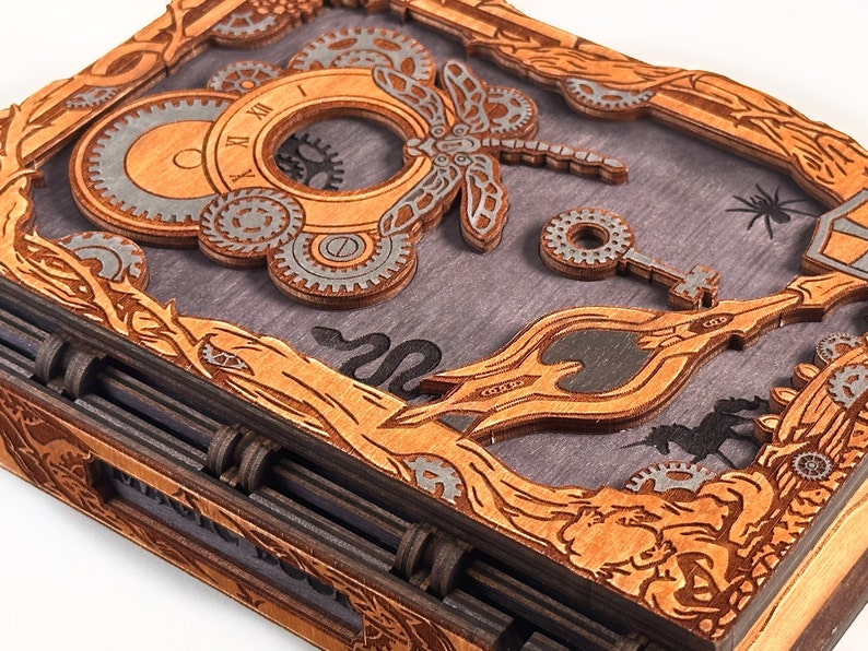 May include: A wooden box with a steampunk design featuring gears, a dragonfly, and a key. The box is closed and has a dark wood finish.