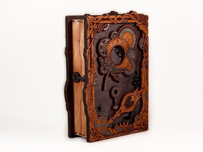 May include: A wooden book box with intricate carvings and a steampunk design. The box features a dragonfly, gears, and a keyhole. The box is made of dark brown wood with a light brown interior.