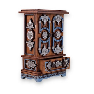 May include: A small wooden cabinet with intricate carvings and a blue and silver painted design. The cabinet has two doors and a drawer.