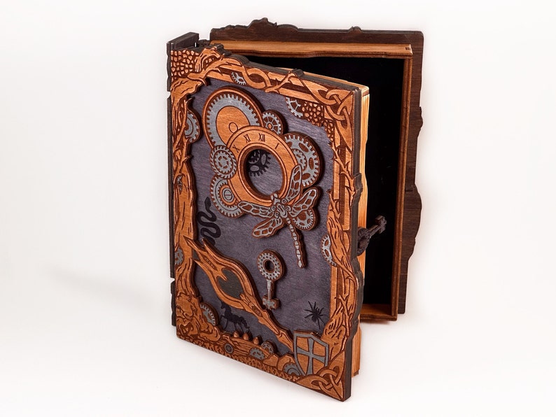 May include: A wooden box with a hinged lid, intricately carved with a steampunk design. The lid features a dragonfly, gears, and a clock face. The box is painted in shades of brown and gray.