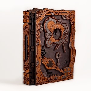 May include: A wooden book with a steampunk design. The cover features a dragonfly, gears, and a keyhole. The book is closed and has a brown and black color scheme.