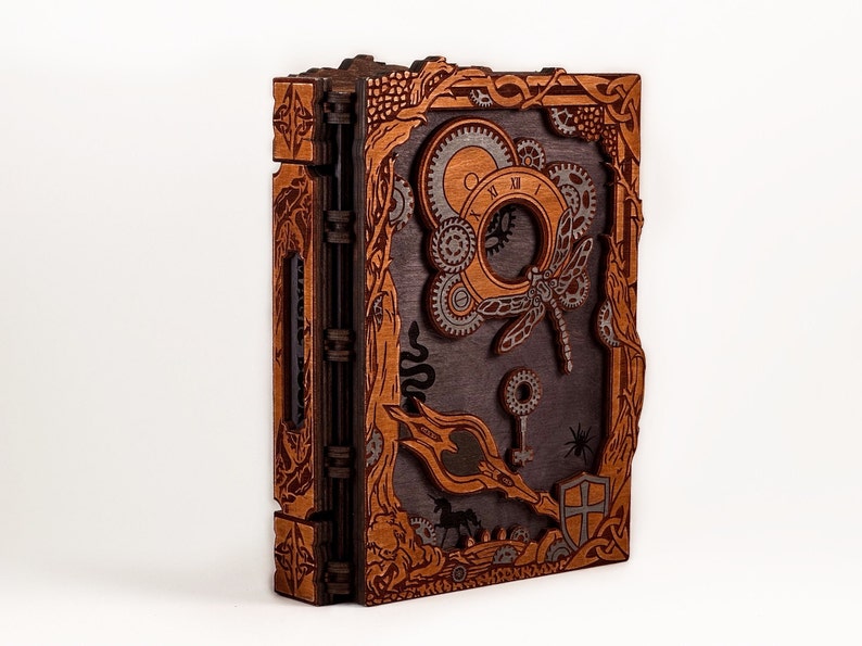 May include: A wooden book with a steampunk design. The cover features a dragonfly, gears, and a keyhole. The book is closed and has a brown and black color scheme.