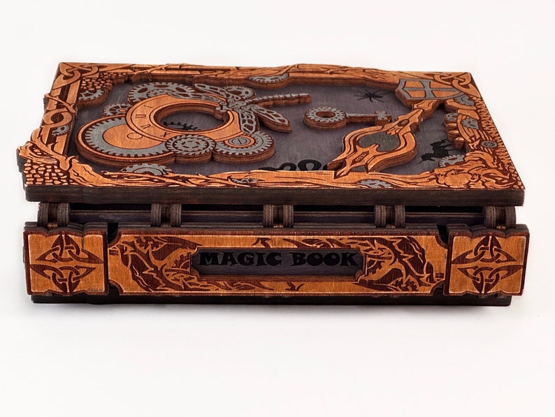 May include: A wooden box with a dark brown finish and intricate carvings. The top of the box features a steampunk design with gears, a dragonfly, and a clock face. The front of the box has the words "MAGIC BOOK" engraved on it.