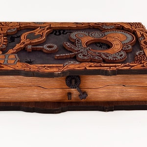 May include: A wooden box with a hinged lid, featuring a steampunk design with intricate gears, a butterfly, and a keyhole. The box is made of dark wood with a light wood interior.