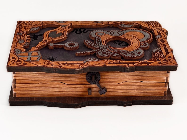 May include: A wooden box with a hinged lid, featuring a steampunk design with intricate gears, a butterfly, and a keyhole. The box is made of dark wood with a light wood interior.