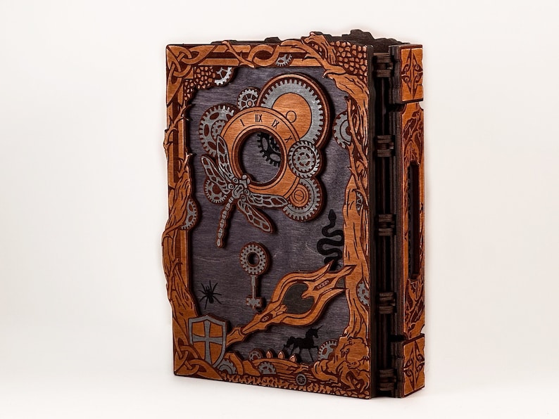 May include: A wooden journal with a steampunk design. The cover features a dragonfly, gears, and a keyhole. The journal is bound with a dark brown leather spine.