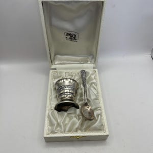 May include: A silver egg cup and spoon set in a white box with a satin lining. The box has the name "Gouviers" printed on it.