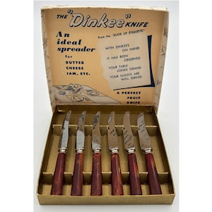 Puede incluir: Un juego de seis cuchillos de tono plateado con mangos jaspeados en rojo oscuro, presentados en una caja de cartón etiquetada The Dinkee Knife. El interior de la caja incluye texto que describe los cuchillos como esparcidores y cuchillos para fruta.