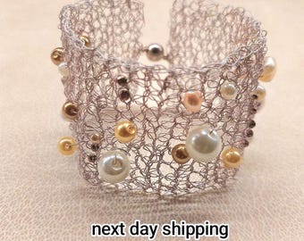 May include: A wide cuff bracelet crafted from fine silver-toned wire mesh, featuring an open-work structure adorned with scattered beads in shades of cream, gold, and bronze. The bracelet includes a small, round silver-toned magnetic clasp.