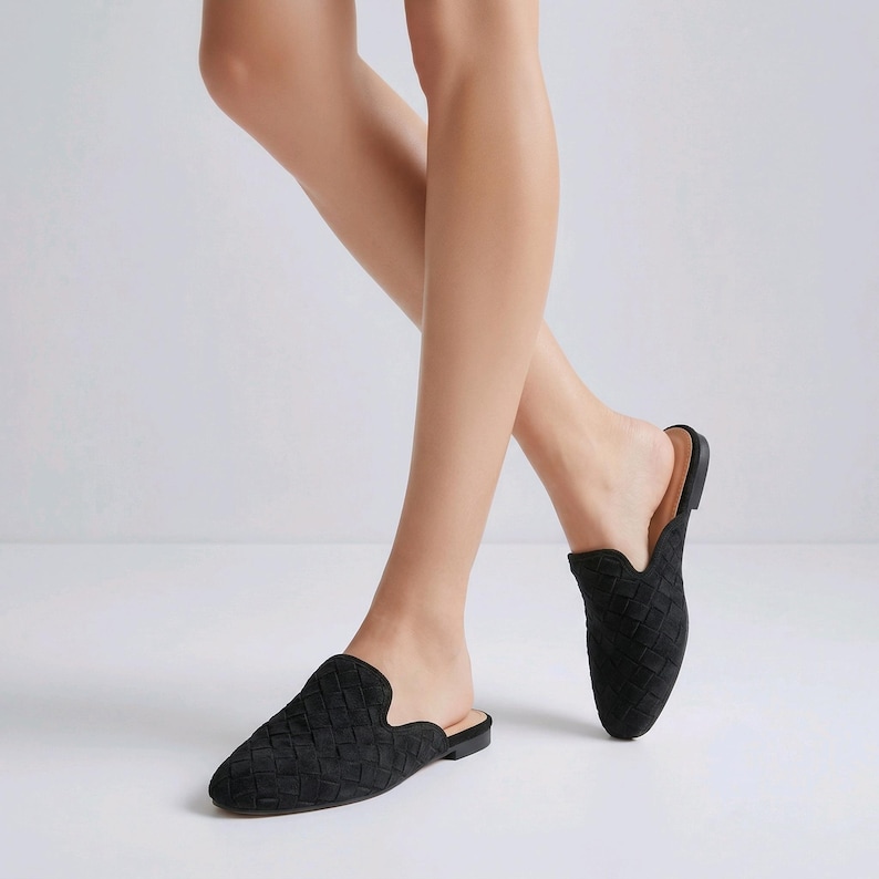May include: Black woven-patterned slip-on mules. The shoes have a pointed toe and a low heel. The open-back design allows for easy wear. The shoes are made of a soft, textured material.
