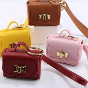 Può includere: Quattro mini borse a mano nei toni del marrone, giallo, rosa e bordeaux. Ogni borsa presenta un manico superiore, una chiusura color oro e un cinturino da polso abbinato. Le borse sono progettate per essere portachiavi.