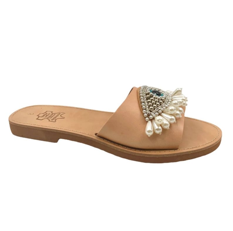 May include: A single beige leather slide sandal with a decorative embellishment. The embellishment features a central blue gem surrounded by silver beads and white pearl-like drops. The sandal has a flat sole.