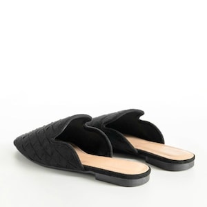 May include: A pair of black woven-patterned mules. The shoes have a pointed toe and a low heel. The interior is a light tan color, and the soles are black. The shoes are set against a white background.