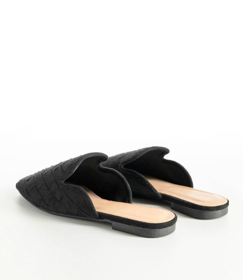 May include: A pair of black woven-patterned mules. The shoes have a pointed toe and a low heel. The interior is a light tan color, and the soles are black. The shoes are set against a white background.