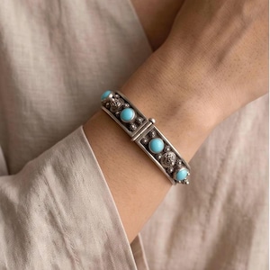 May include: A hinged silver cuff bracelet featuring four round, smooth, light blue turquoise stones set in metal frames. The silver band is decorated with small, raised star-like patterns and circular metal accents surrounding each stone.